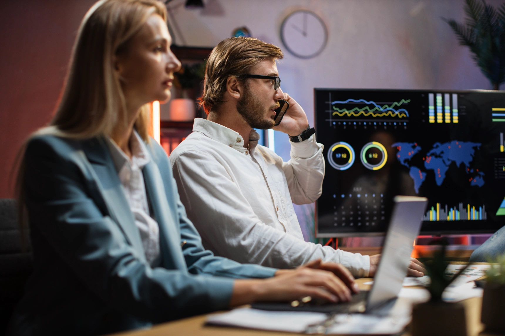 Analysts in a dark operations room monitoring data dashboards, one speaking on the phone.