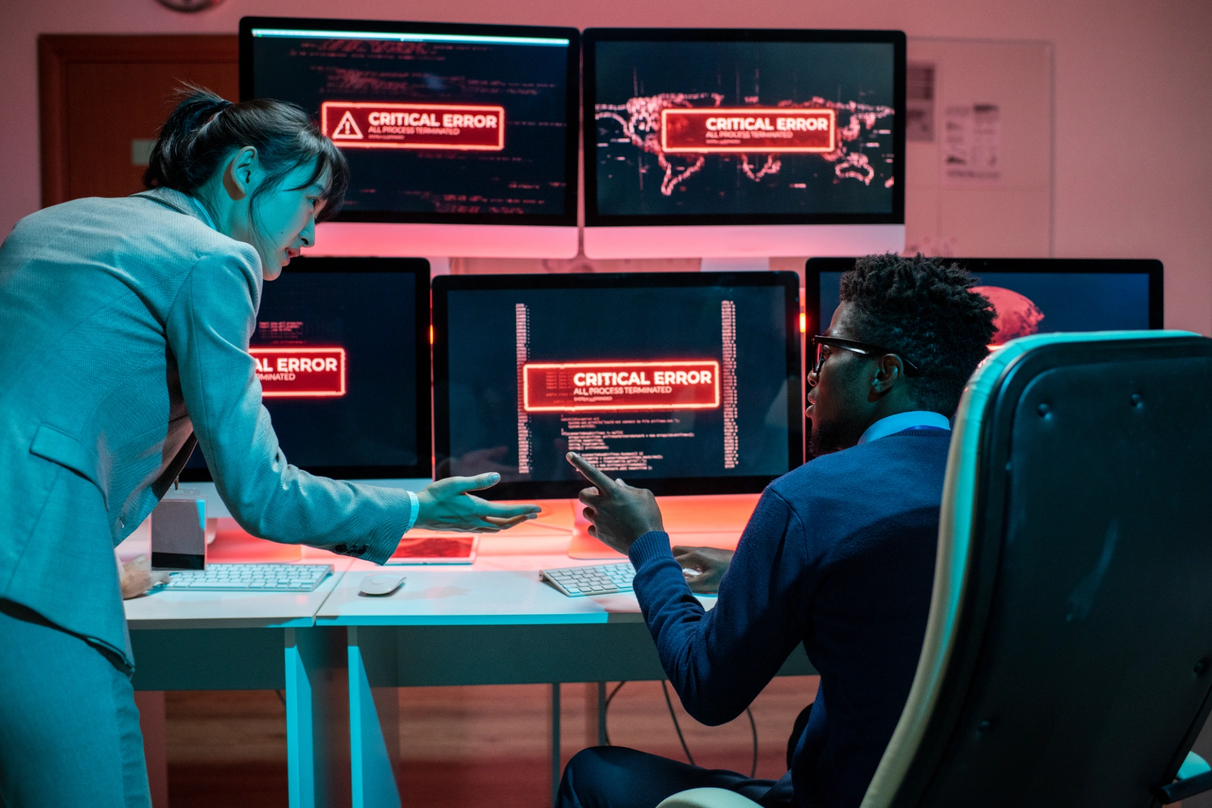 Two cybersecurity professionals reacting to critical error messages on multiple monitors.