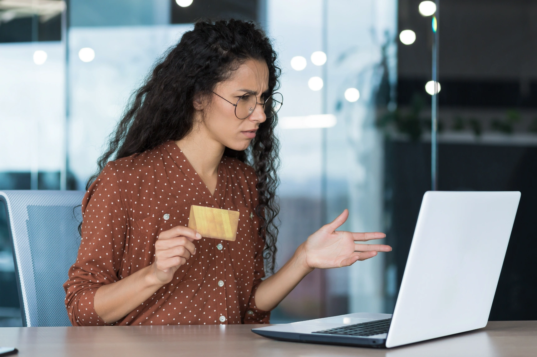 Frustrated woman holding a credit card while looking at her laptop screen.