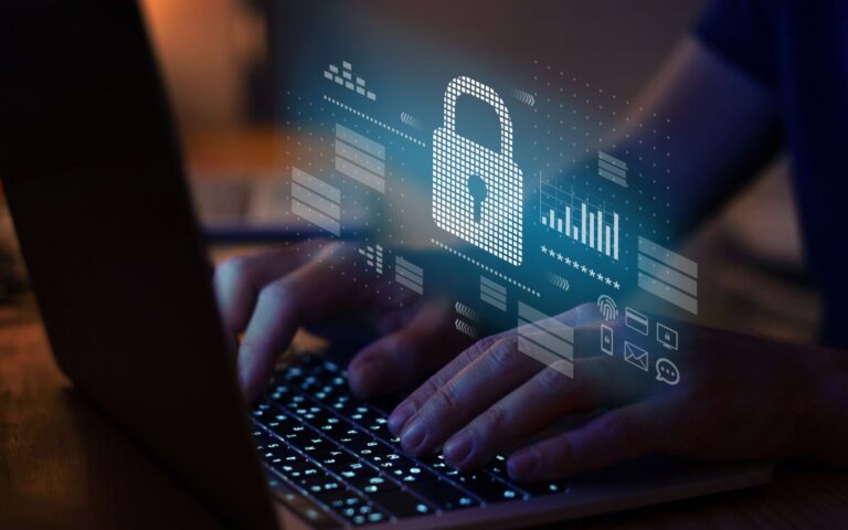 Cybersecurity image of hands typing on a laptop with a holographic lock icon and security data, symbolizing digital protection.