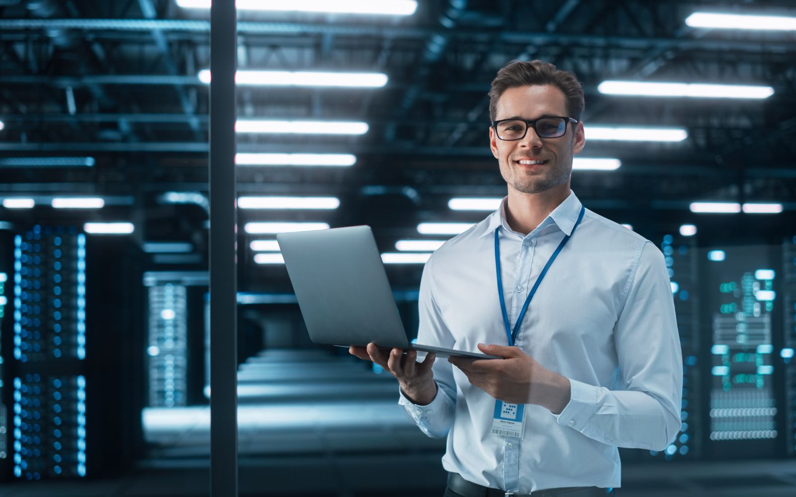 IT professional image of a man in a data center holding a laptop, smiling, with server racks in the background.