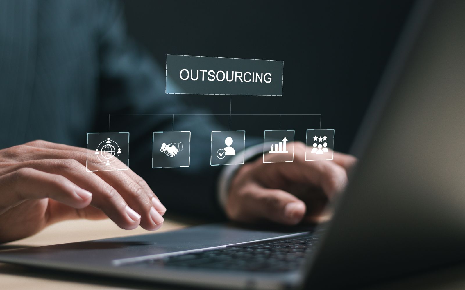 IT outsourcing image of hands on a laptop with a holographic interface displaying icons for global reach, collaboration, and growth. benefits of outsourcing it services
